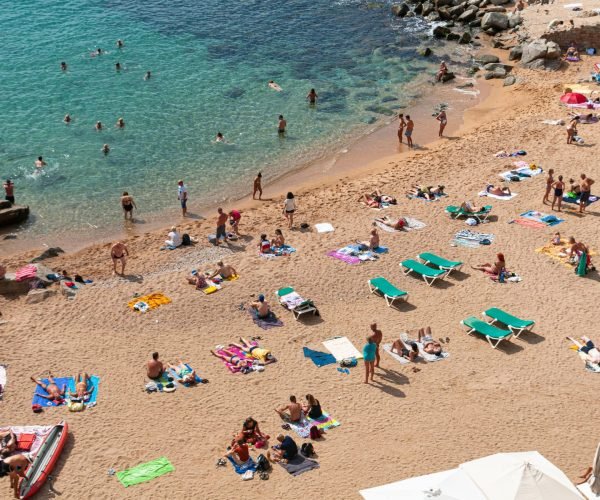 pexels-photo-14283395-14283395 Crowded beach scene in Tossa de Mar, Spain with sunbathers and swimmers enjoying a sunny day.