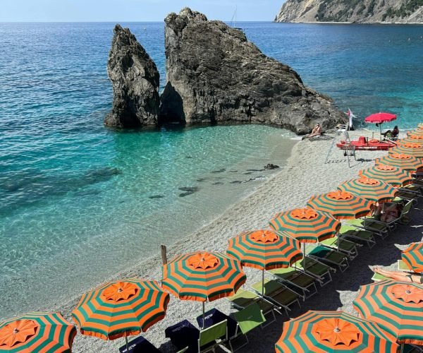 pexels-photo-17382364-17382364 Colorful beach umbrellas on an Italian coast with rocky formations and turquoise sea.