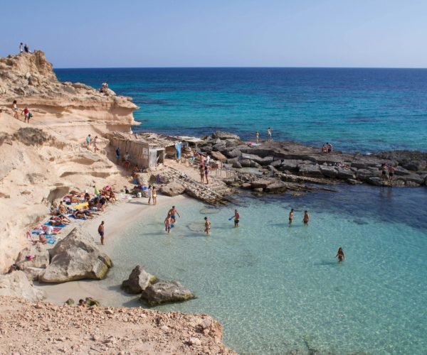 Stunning coastline photo capturing beachgoers at a rocky cove in Illes Balears, Spain.