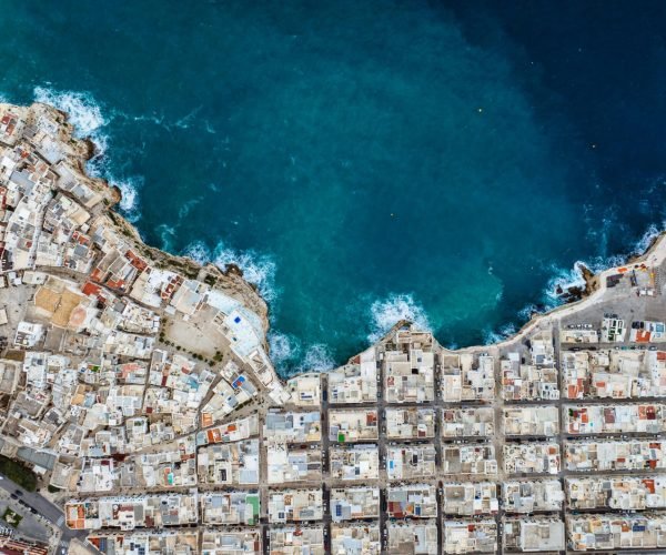 Drone shot of Polignano a Mare showcasing urban coastline against the blue sea.