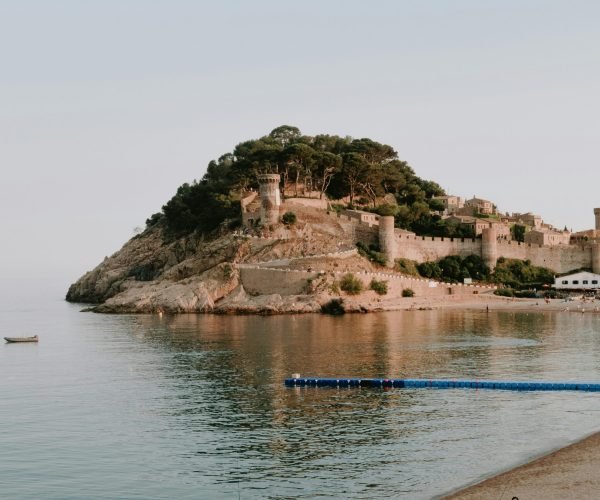 Beautiful view of a medieval castle on the Costa Brava coast with calm sea and sandy beach.