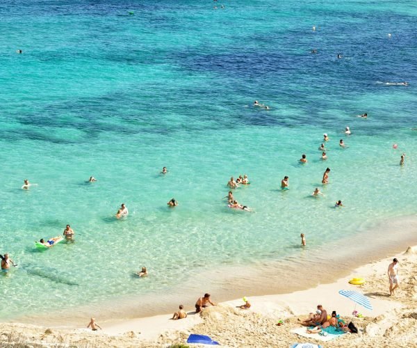 People enjoying a sunny day at a beautiful beach in Mallorca, Spain, with turquoise water and sandy shores.